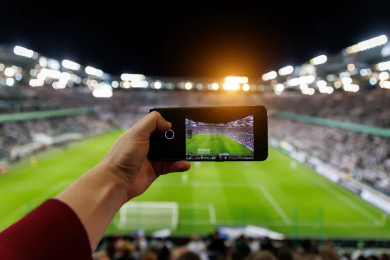 Fan hand with smartphone photographing football match. Using mobile phone camera at the stadium